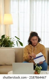 Worried Schoolgirl Sitting On Sofa At Home And Opening Letter From University