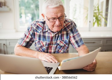 Worried Senior Man Looking At A Document While Using Laptop