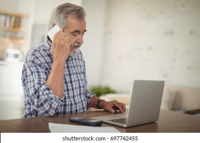 Worried Senior Man Taking On Phone While Using Laptop At Home