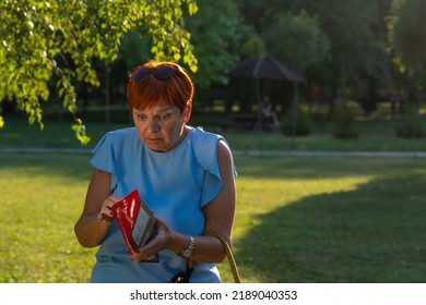 Worried Senior Red Haired Woman Is Looking At An Empty Wallet. Unhappy Bankrupt Woman With Empty Wallet. Mature Woman Shows Her Empty Wallet. Bankruptcy, Stagflation, Inflation