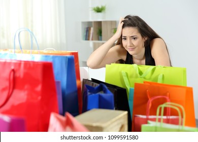 Worried shopaholic woman after multiple purchases in colorful shopping bags at home
