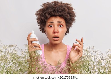 Worried Sick Woman Suffers From Allergic Rhinitis Holds Aerosol Spray Has Red Itchy Eyes Surrounded By Wildflowers Isolated Over White Background. Female Has Blocked Nose Because Of Allergy.