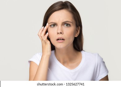 Worried stressed teen girl checking crows feet troubled with wrinkles on face looking at camera, upset depressed young woman confused about facial skin problem isolated on studio background, portrait