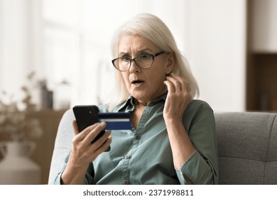 Worried surprised elderly woman in glasses looking at smartphone and credit card, getting financial problems, bad online bank service, finding overspending, bankruptcy risk - Powered by Shutterstock