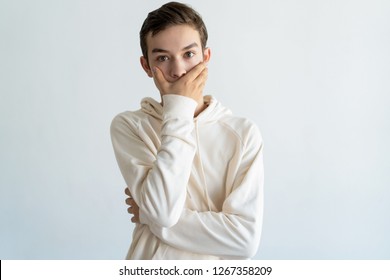 Worried Teen Boy Covering Mouth With Hand. Embarrassed Handsome Young Guy Looking At Camera. Bewilderment Concept. Isolated Front View On White Background.