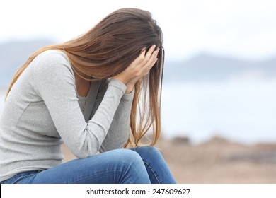Worried teenager woman covering her face with hands on the beach in winter