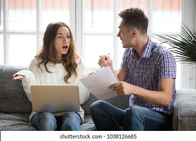 Worried unhappy couple arguing about debt or high domestic bills with laptop and documents, young family having quarrel discussing wasting money bankruptcy problem sitting together on sofa at home