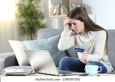 Worried woman buying with laptop and credit card sitting on a couch in the living room at home