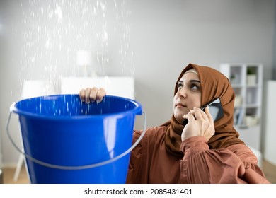 Worried Woman Calling Plumber While Collecting Water Droplets Leaking From Ceiling At Home