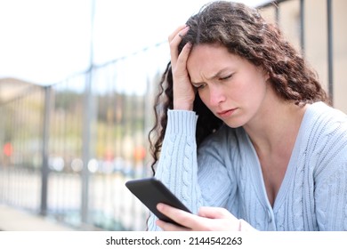 Worried woman checking cell phone sitting in the street