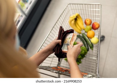 Worried woman checking her wallet when shopping in supermarket. Inflation and economic recession concept.