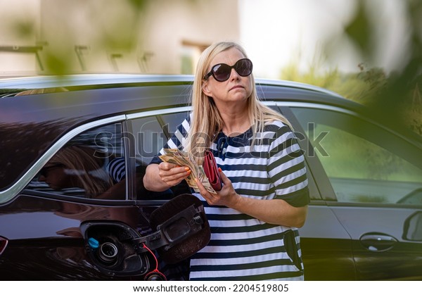 worried woman with euro cash at the\
car, put money to car tank, the concept of rising fuel\
prices