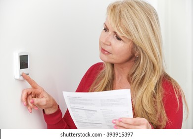 Worried Woman With Heating Bill Turning Down Thermostat