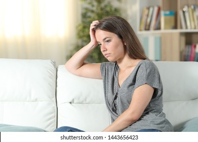 Worried woman looking away sitting on a couch in the living room at home - Shutterstock ID 1443656423