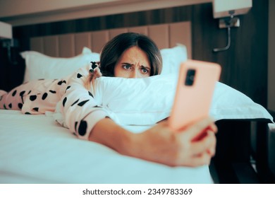 
Worried Woman Looking at her phone Lying in Bed. Depressed girl being chronically online upset about cyberbullying 
