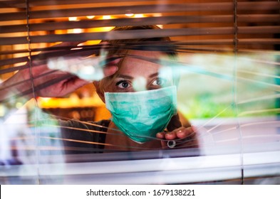 Worried Woman looking through window from home in quarantine during Coronavirus. Anxiety Woman in self distancing isolation due to Covid-19.Stay at home in time of pandemic concept 
