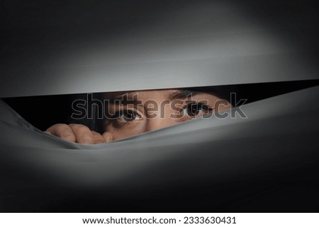 Worried woman looking through window blinds into darkness. Paranoia concept