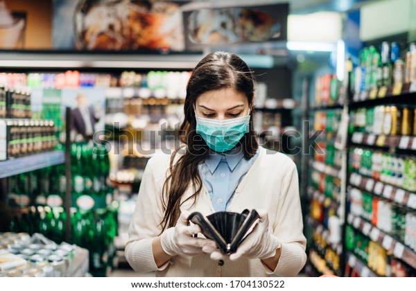 Worried woman with mask groceries shopping in\
supermarket looking at empty wallet.Not enough money to buy\
food.Covid-19 quarantine lockdown.Financial problems\
anxiety.Unemployed person in money\
crisis