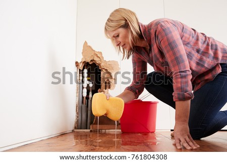 Worried woman mopping up water from a burst pipe with sponge