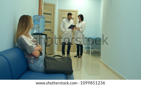 Worried woman patient waiting in hospital hall while two doctors discussing diagnosis