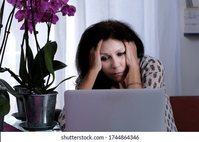 Worried Woman Sitting In Front Of Computer. Vase With Pink Orchids On The Left