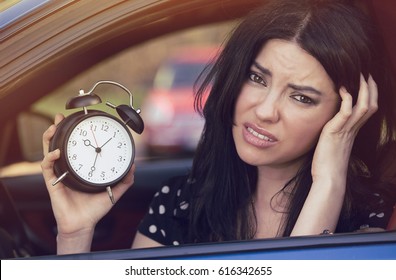 Worried Woman Sitting Inside Her Car Showing Alarm Clock Running Late To Work