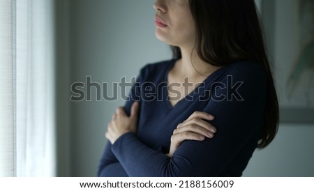 Worried woman standing by window touching her neck and chest seeking comfort. Thoughtful preoccupied person
