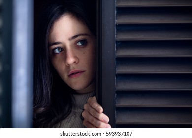 Worried Woman Watching Outside from a Wooden Window Shutter