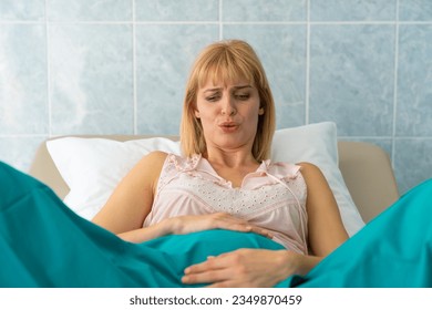 Worried young adult blonde Caucasian woman giving birth in private hospital holding her belly with both hands and breathing. - Powered by Shutterstock