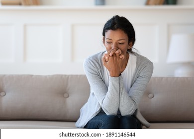Worried young african american woman sitting on sofa, thinking of personal problems alone indoors, copy space. Unhappy mixed race lady feeling frustrated or nervous, suffering from loneliness.