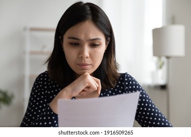 Worried young asian woman sit at desk read official bank notification about debt penalty fee warning of financial problem. Concerned vietnamese business lady dissatisfied by bad news from paper letter