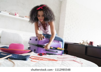 Worried Young Black Woman Packing Bags For Holiday. Girl Trying To Close Full Suitcase For Vacation, Getting Ready For Traveling