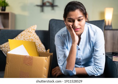 Worried young business woman sitting sadly on sofa at home due to loss of job, employment or fired from the work