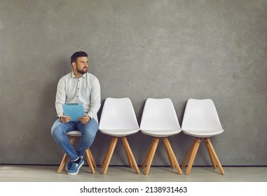Worried young caucasian male job seeker vacancy candidate holding resume form waiting for interview meeting sitting on chair looking aside. Jobless applicant at recruitment staffing agency