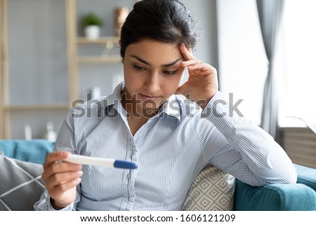 Worried young infertile indian woman holding pregnancy test negative result feel anxious sit on sofa alone at home, upset pregnant ethnic teen girl depressed about unwanted pregnancy concept regret Stock photo © 
