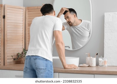 Worried young man with hair loss problem looking in mirror at home - Powered by Shutterstock