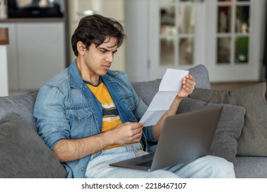 Worried Young Man Reading Paper Bill Pay Online Using Mobile Phone At Home. Male Holding Bank Letter Reading Bad News, Planning Loan Debt 