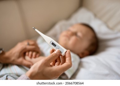 Die bekümmerte junge Mutter saß neben ihrem kranken Sohn mit hohem Fieber auf dem Sofa. Mutti misst die Temperatur mit dem Thermometer kranken Kindes, das zu Hause unter einer Decke liegt.