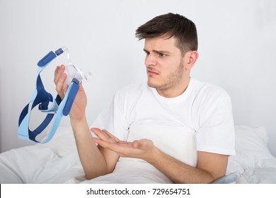 Worried Young Patient Looking At CPAP Machine On Bed