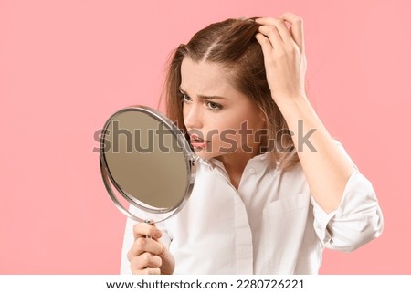 Worried young woman with hair loss problem and mirror on pink background