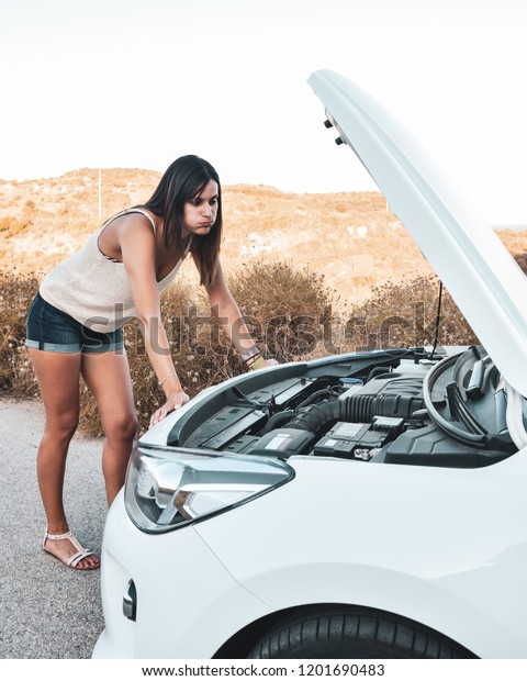 Worried young woman looking at the engine of her\
broken down car