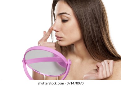 worried young woman raises her nose with a finger in front of the mirror