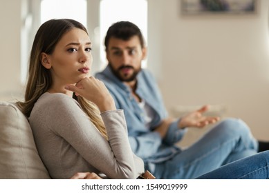 Worried young woman sitting on sofa at home and ignoring her boyfriend who is sitting next to her - Shutterstock ID 1549019999