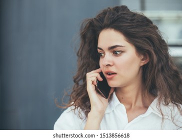 Worried young woman stand outside and talk on phone. Look at left and hold smartphone close to ear. Alone on street. Modern view