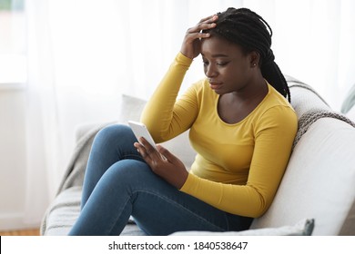 Worry African American Female Looking At Smartphone Screen At Home, Reading Bad Message, Upset Black Woman Received Unpleasant News By Phone, Sitting On Couch With Cellphone In Hands, Free Space