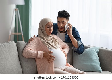 Worry Muslim Husband Calling Emergency While His Pregnant Wife Having Prenatal Contractions At Home. Islamic Expecting Mother In Hijab Suffering Painful Spasms And Spontaneous Labour, Copy Space - Shutterstock ID 1901153500
