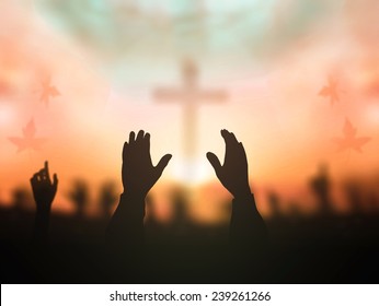 Worship God concept: Silhouette person hands reaching over blurred cross autumn sunset background