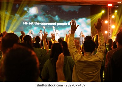 Worship includes music and numerous people lifting their hands in praise to God on stage  - Shutterstock ID 2327079459