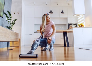 Worthy Caucasian Blond Housewife Crouching In Living Room And Using Steam Cleaner To Clean Parquet.