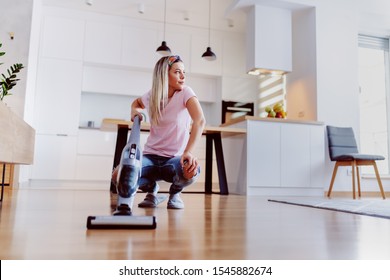 Worthy Caucasian Blonde Housewife Steamer To Clean Floor In Living Room While Crouching And Looking Away.